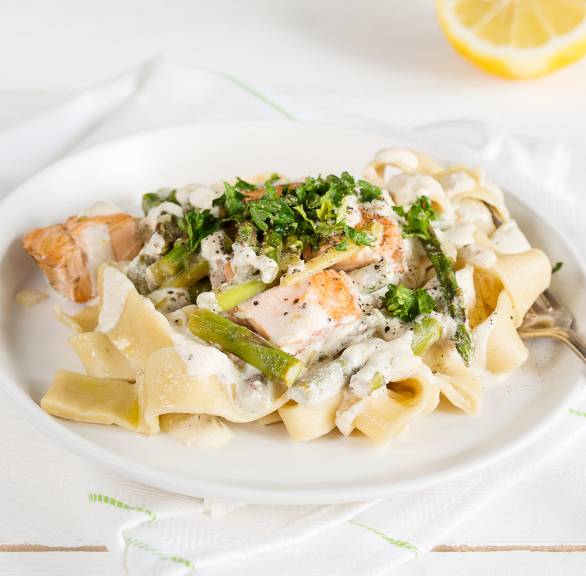 Bandnudeln mit Lachsfilet, grünem Spargel und Sahnesauce auf einem Teller getoppt mit frischer Petersilie