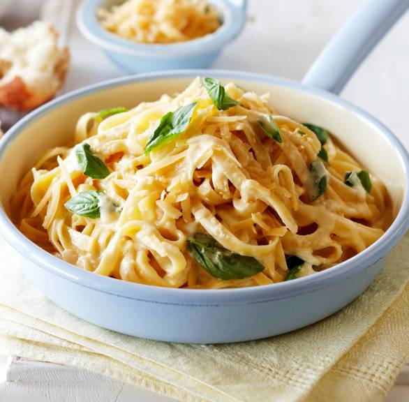 Pasta Alfredo in einer Stielpfanne getoppt mit Käse und frischem Basilikum