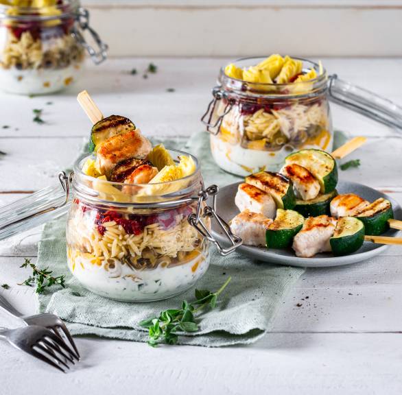 Pastasalat im Glas geschichtet, darauf Spieße mit gegrilltem Hähnchen und Zucchini
