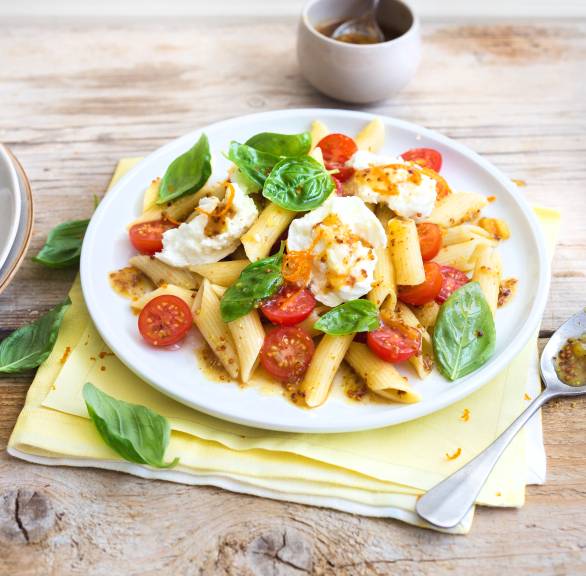 Pastasalat aus Röhrennudeln auf einem Teller, darauf Kirschtomaten, Mozzarella und Orangen-Senf-Dressing in einer Schüssel daneben