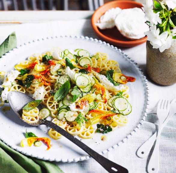 Pastasalat mit Zucchini und Zucchiniblüten auf einem Teller, getoppt mit Mozzarella, Basilikum und Minze