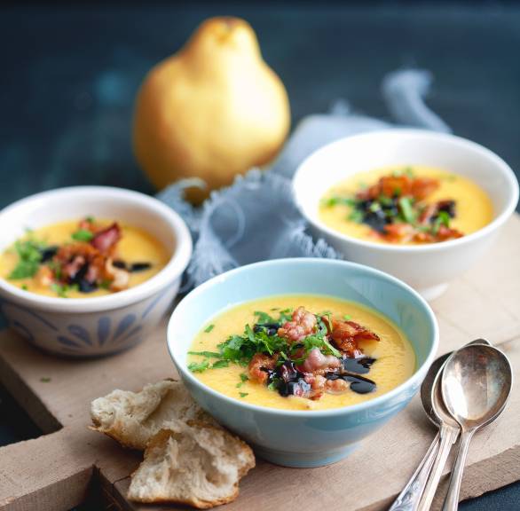 Quittensuppe mit Pastinaken angerichtet in drei Suppentellern getoppt von Speckstreifen und Balsamicoessig