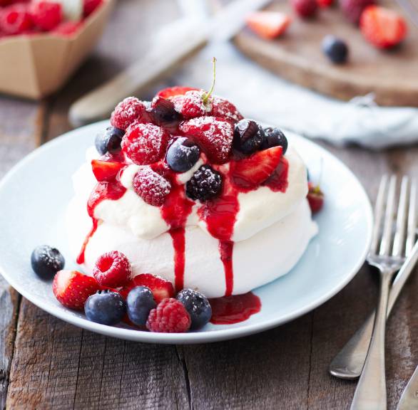 Mini-Pavlova mit frischen Beeren und Himbeeressigsauce auf einem Dessertteller