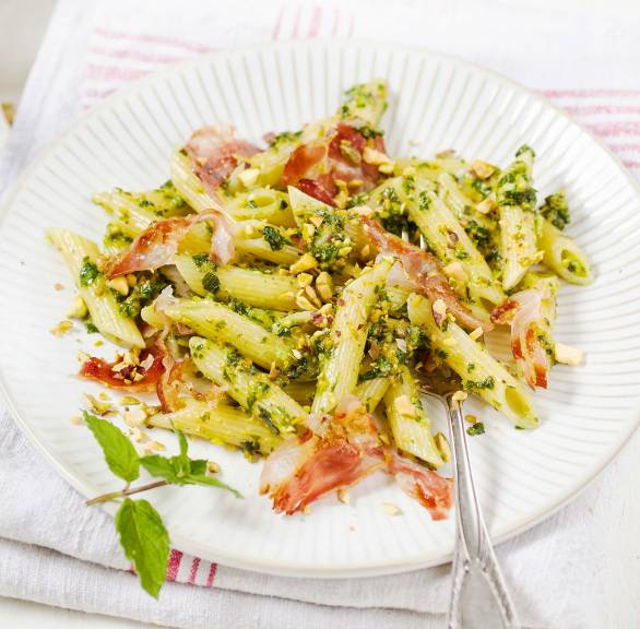 Penne mit Pistazienpesto und gebratenem Pancetta auf einem Teller angerichtet