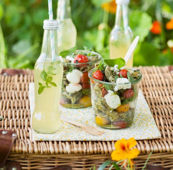 Nudelsalat in zwei Gläsern auf einem Gartentisch, daneben zwei Flaschen Limonade