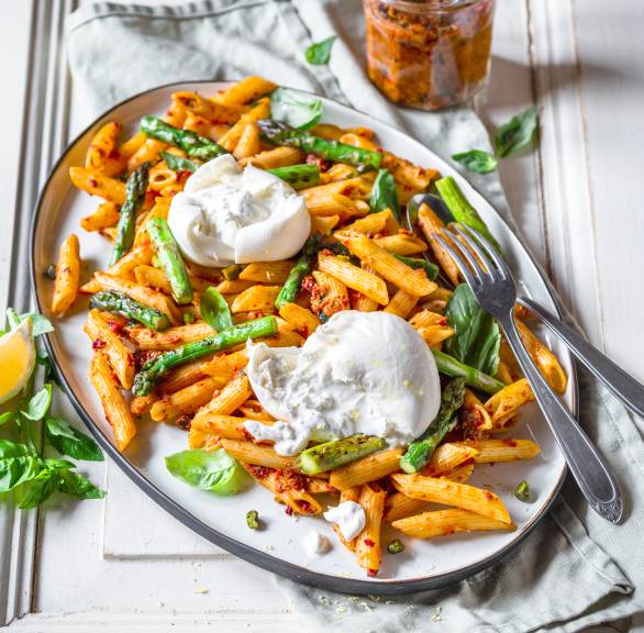 Nudelsalat aus Penne mit grünem Spargel auf einem ovalen Teller getoppt von Burratakugeln
