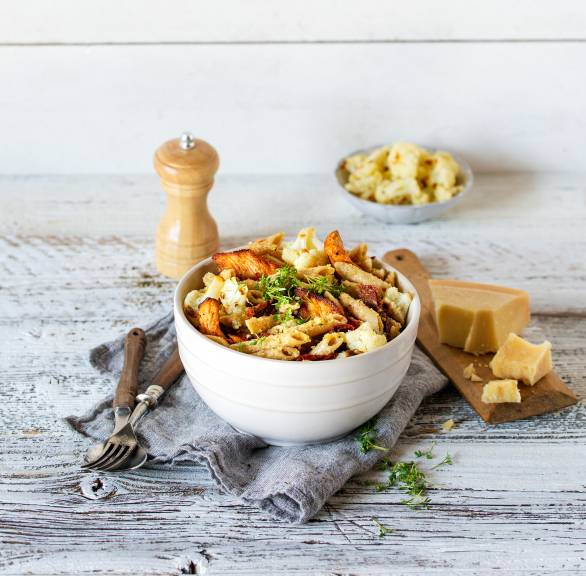Salat mit Vollkornpenne in einer Schüssel getoppt von Hähnchenstreifen, daneben ein Stück Parmesan