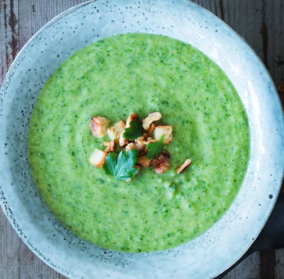 Wirsingcremesuppe in einem Teller getoppt von Croûtons,  Nüssen und frischer Petersilie auf einem Tisch von oben