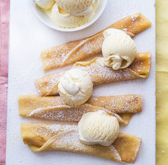 Pfannkuchen aufgerollt nebeneinander auf einem Teller getoppt von Vanilleeis