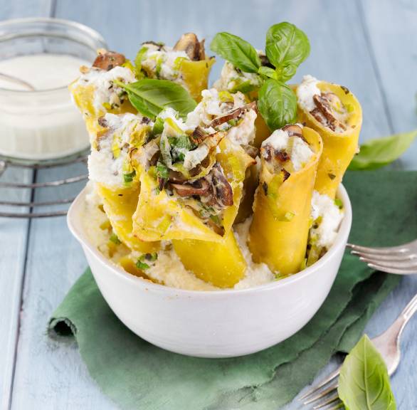 Cannelloni mit Champignon-Lauch-Ricotta-Füllung aufrecht angerichtet in einer Schale garniert mit frischem Basilikum
