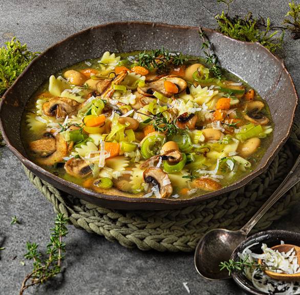 Champignon-Minestrone mit Gemüse, Bohnen und Nudeln in einer Suppenschale auf einem Tisch