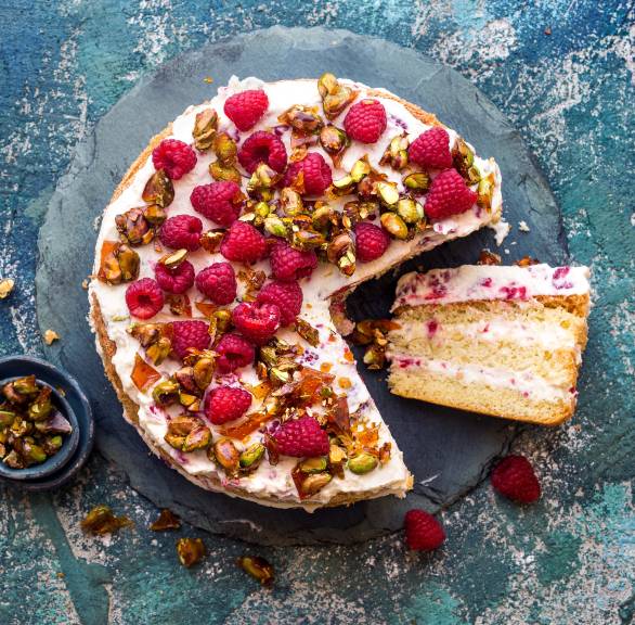 Pistazien-Himbeer-Torte angeschnitten auf einer Tortenplatte garniert mit frischen Himbeeren und Pistazienkernen