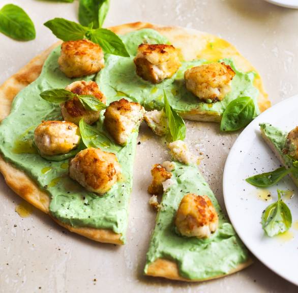 Runde Pizza mit Basilikumcreme und Fischbällchen angeschnitten auf einem Tisch