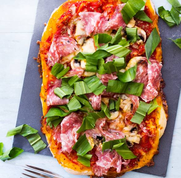 Pizza belegt mit Champignons, Salami und frischem Bärlauch auf einem Schieferbrett