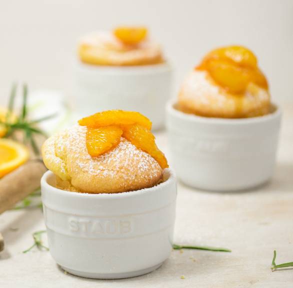 Drei süße Polentaküchlein in Mini-Backformen getoppt mit Rosmarin und Orangenkompott auf einem Tisch