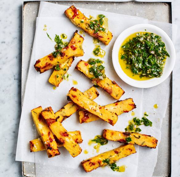Goldbrauen gebackene Polenta-Pommes mit Feta auf einem Backblech getoppt von grüner Kräuter-Salsa