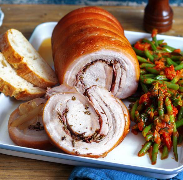 Porchetta, gefüllter Schweinerollbraten auf einem rechteckigen Teller, daneben Bohnengemüse