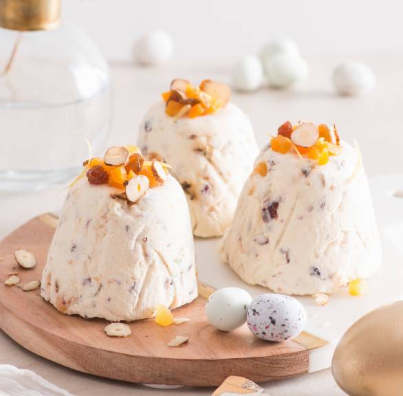 Drei Quark-Desserts in Törtchenform mit Trockenfrüchten und Nüssen auf einem runden Holzbrett mit Osterdeko