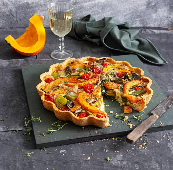 Kürbisquiche angeschnitten auf einer Schieferplatte, dahinter ein Stück Hokkaido