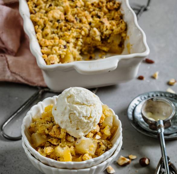 Quitten-Apfel-Crumble mit Haselnüssen und Vanilleeis auf einem Tisch