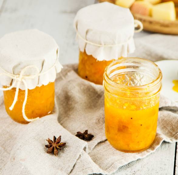 Quittenmarmelade in Einmachgläsern auf einem Tisch, daneben Kürbis und Käse