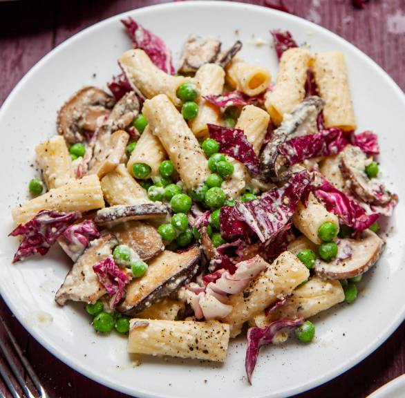 Rigatoni in Sahnesoße mit Erbsen, Radicchio und zwei Sorten Pilzen angerichtet auf einem Teller