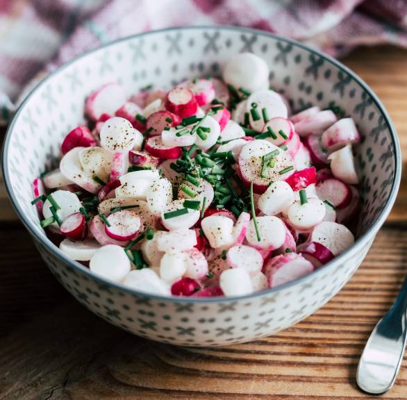 Radieschensalat in einer Salatschüssel getoppt mit Joghurt-Dressing auf einem Tisch