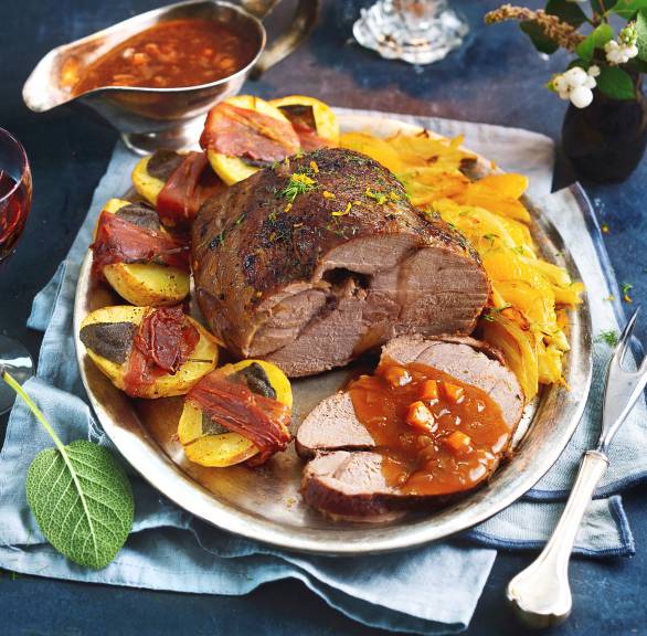 Geschmorter Rehbraten angerichtet auf einer Servierplatte umgeben von Saltimbocca-Kartoffeln, Fenchelgemüse und Rotweinsoße