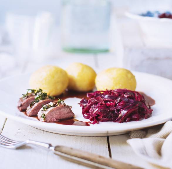 Rehrückenscheiben zusammen mit Rotkohl, Polentaknödeln und Portweinsoße auf einem weißen Teller