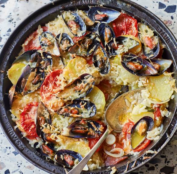 Reis-Kartoffel-Auflauf nach apulischer Art mit Muscheln in einer runden Auflaufform auf einem Tisch