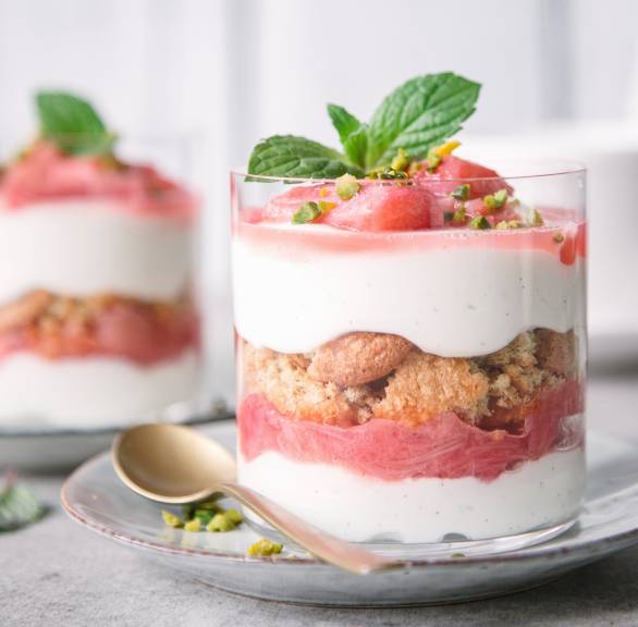 Rhabarber-Tiramisu mit Biskuit in zwei Dessertgläser geschichtet garniert mit frischer Minze auf einem Tisch