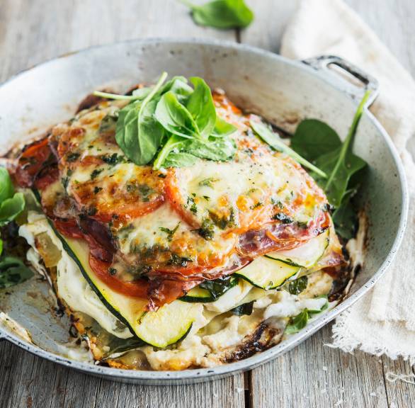 Ein Stück Zucchini-Ricotta-Lasagne mit Schinken angerichtet mit frischem Basilikum auf einem Teller