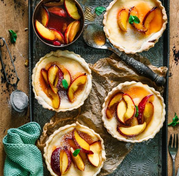 Vier Tartelettes gefüllt mit Ricottacreme und Nektarinen auf einem Backblech von oben