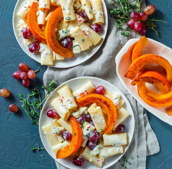 Rigatoni auf zwei Tellern getoppt von Gorgonzolasoße, dunklen Trauben und Kürbisspalten