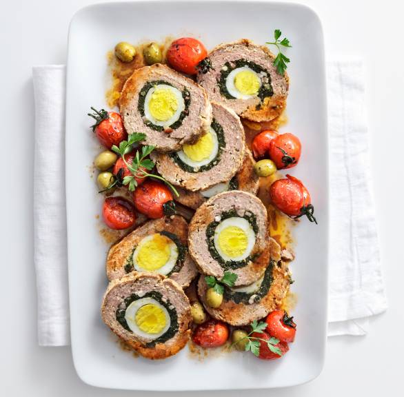 Rinderhackbraten alla pasqualina in Scheiben geschnitten angerichtet auf einer Servierplatte mit Kirschtomaten und Oliven