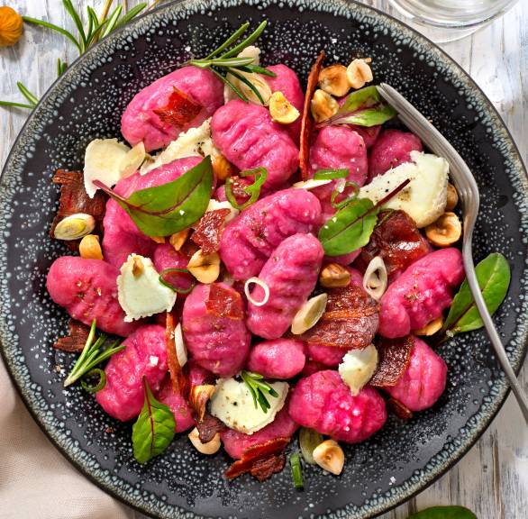 Selbstgemachte Rote Bete-Gnocchi mit Ziegenkäse, Pancetta und Haselnüssen angerichtet auf einem Teller