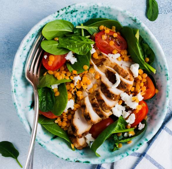 Roter Linsensalat mit Babyspinat und Tomaten getoppt von gegrillter Hähnchenbrust und Dressing in einer Salatschüssel