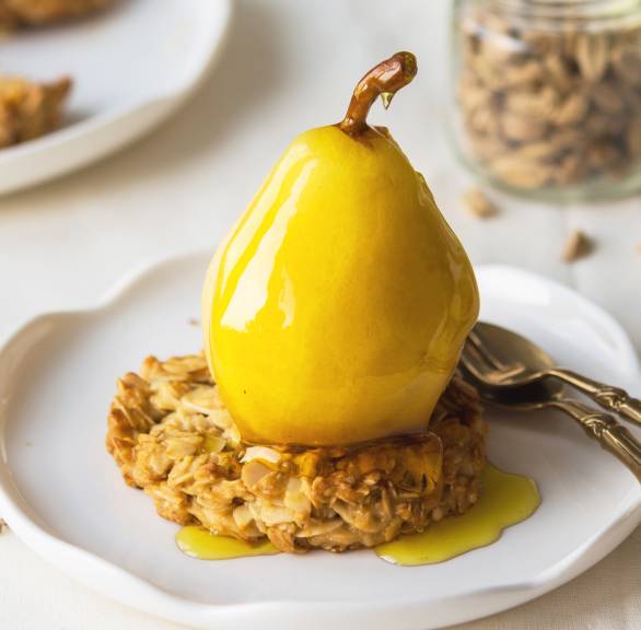 Ganze, pochierte Birne auf einem Haferkeks auf einem Dessertteller übergossen mit Safransud