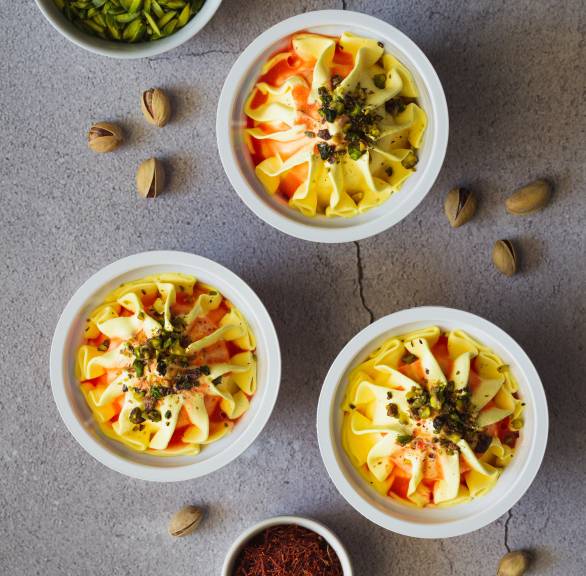 Selbstgemachtes Safran-Eis in drei Dessertschalen auf einem Tisch, daneben Safranfäden und Pistazienkerne