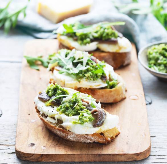 Crostini auf einem Holzbrett getoppt von Sardellenfilets, Mozzarella und grünem Pesto