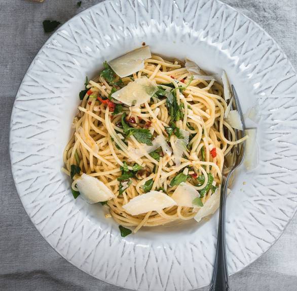 Knoblauch-Spaghetti mit Peperoncini getoppt von Parmesan und frischer Petersilie auf einem tiefen Teller