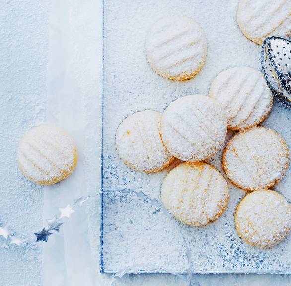 Schneeflöckchen-Plätzchen auf einem rechteckigen Teller, daneben Weihnachtsdeko
