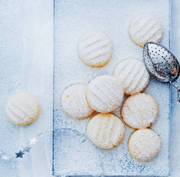 Schneeflöckchen-Plätzchen auf einem rechteckigen Teller, daneben Weihnachtsdeko