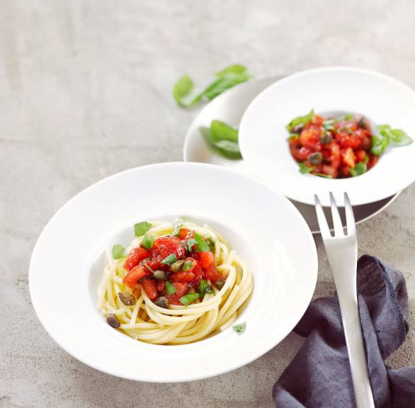 Spaghetti in einem tiefen Teller getoppt mit Tomatentagout und frischen Kräutern auf einem Tisch