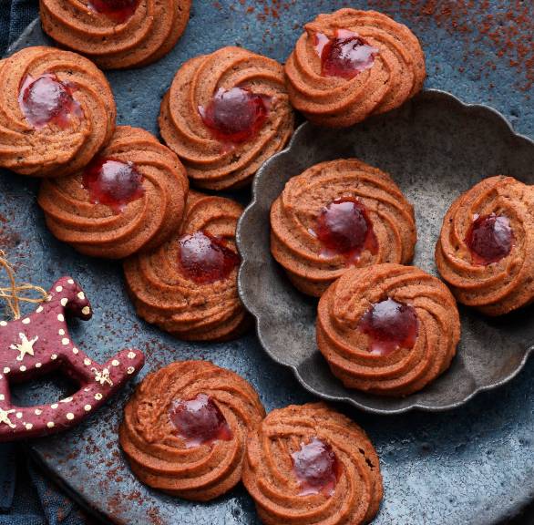 Schoko-Kirsch-Spritzgebäck in Kringeln gebacken auf einem Plätzchenteller, daneben Weihnachtsdeko