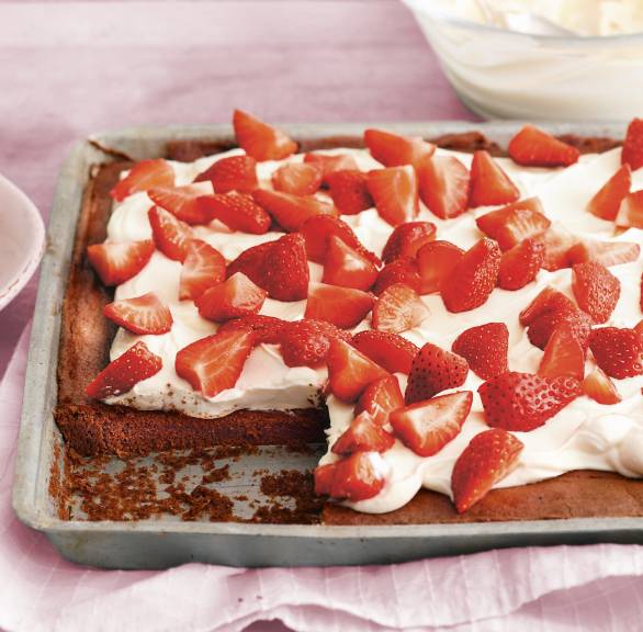 Blechkuchen aus Schokoladenboden getoppt mit mascarponecreme und frischen Erdbeeren angeschnitten auf einem Backblech