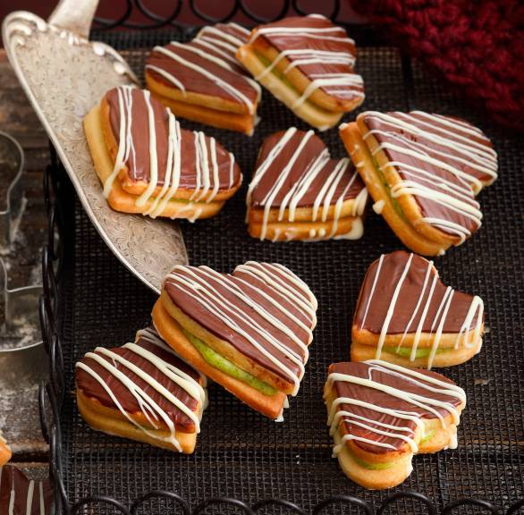 Doppeldeckerplätzchen in Herzform mit Pistazienfüllung und Schokolade auf einem Kuchengitter