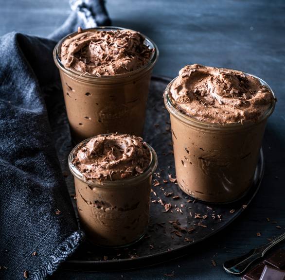  Schokomousse in drei Dessertgläser getoppt von geraspelter Schokolade auf einem festlich dekorierten Tisch