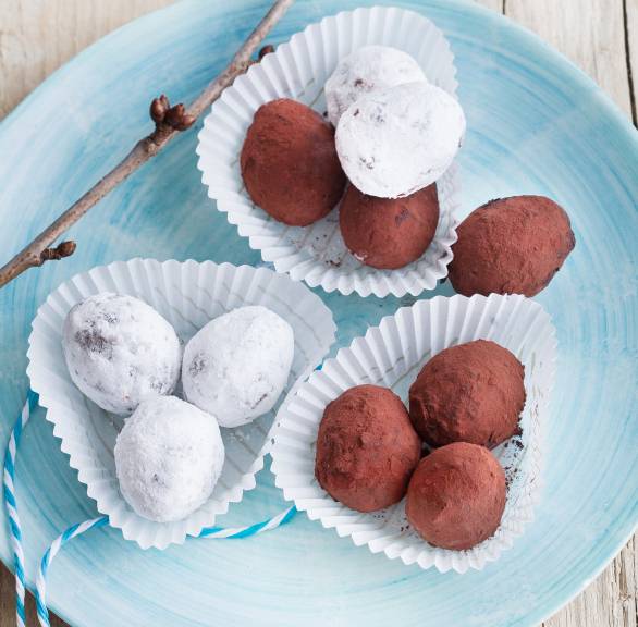 Selbstgemachte Kaffee-Schokotrüffel mit zweierlei Ummantelung angerichtet in Pralinenförmchen auf einem Dessertteller