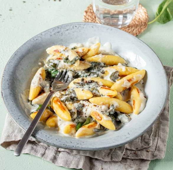 Schupfnudeln mit Spinat-Ricotta-Soße angerichtet auf einem tiefen Teller